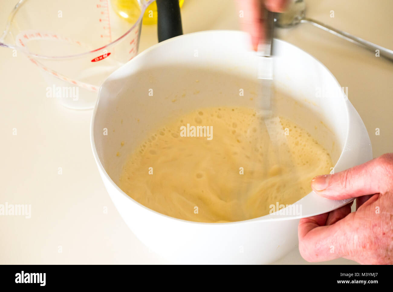Man beating mixture with whisk to make pancake batter for Shrove Tuesday with flour, milk, eggs, and oil in a home kitchen Stock Photo