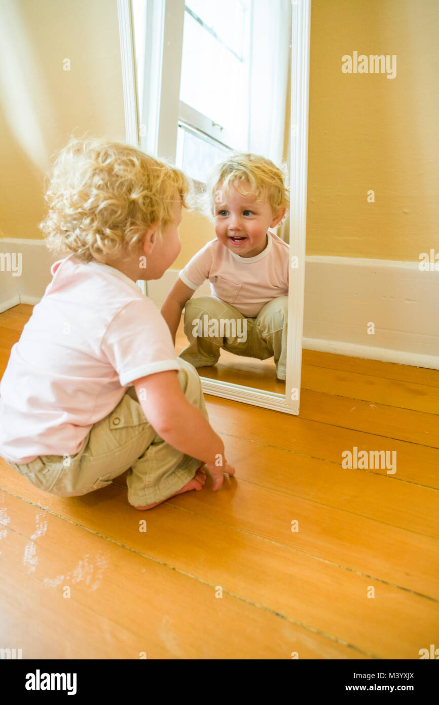 A toddler girl playing and looking at herself in a mirror Stock Photo