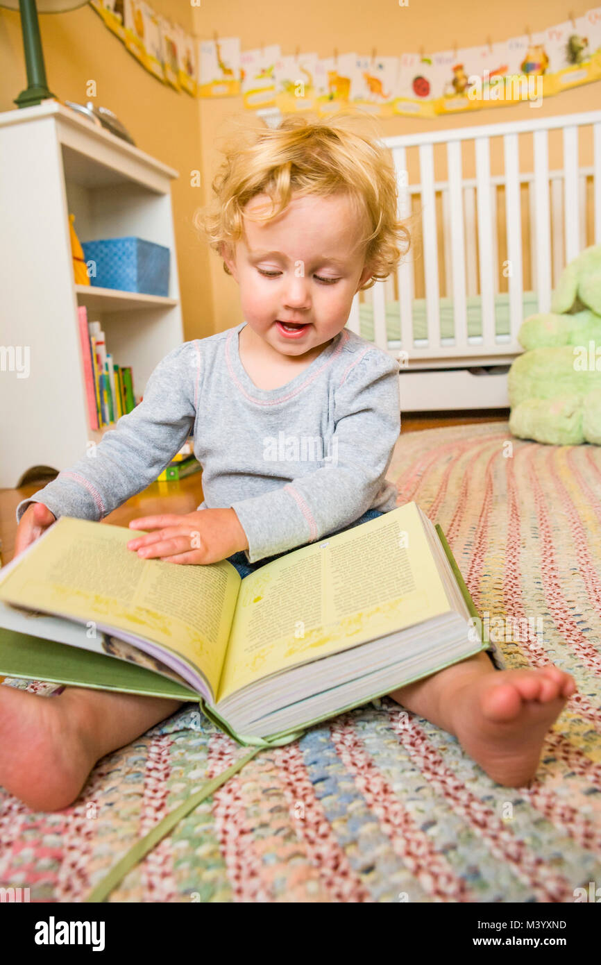 An 18 month old toddler sitting on the floor of her room with a big book Stock Photo Alamy
