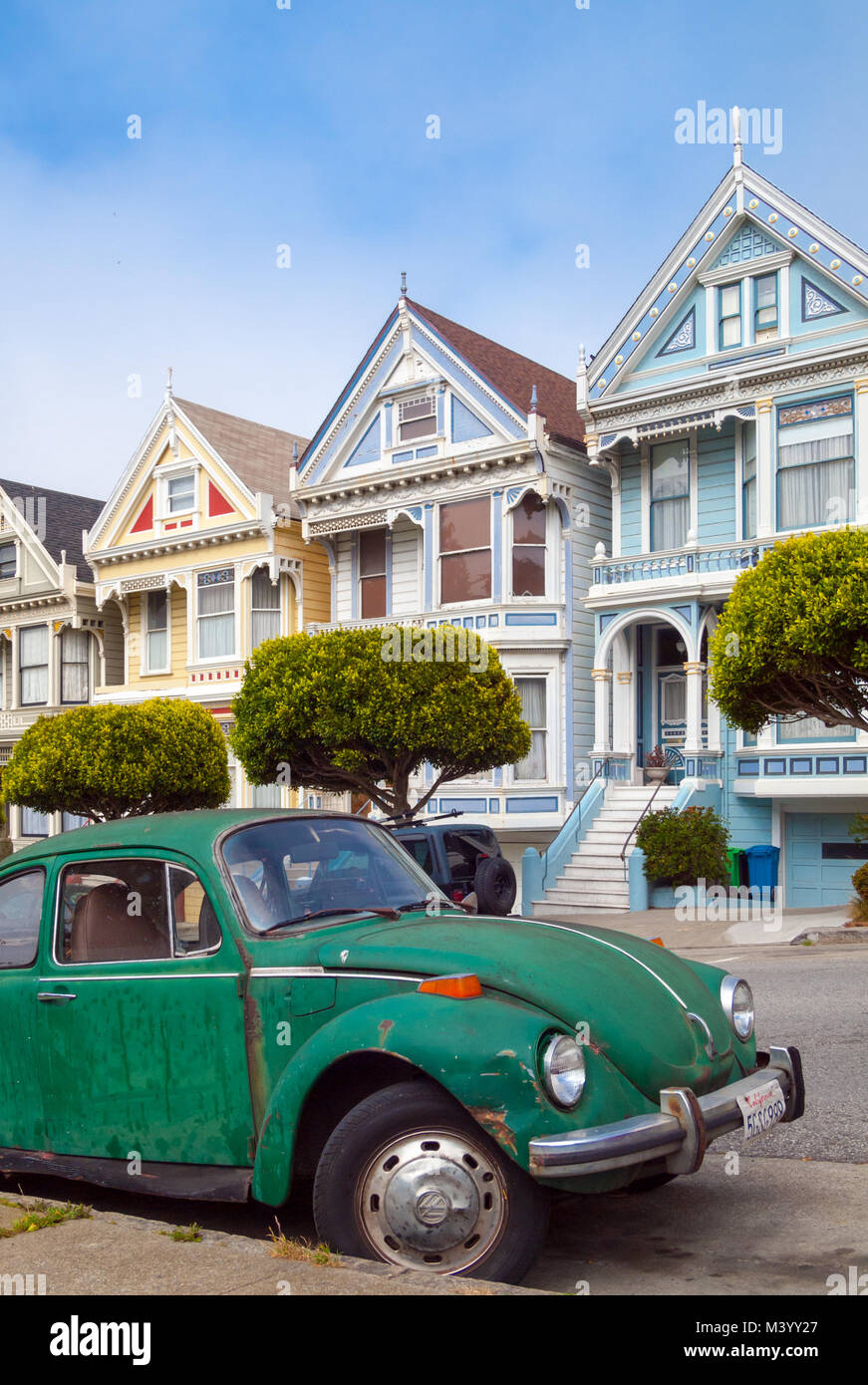A green Volkswagen Beetle parked in front of the 'Painted Ladies' row of Victorian Houses on Steiner Street (at Alamo Square) in San Francisco. Stock Photo