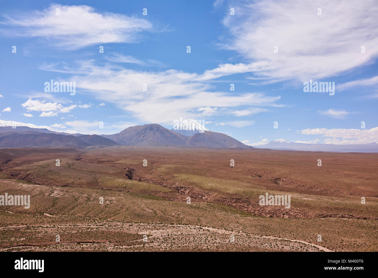 Arid landscape of the Atacama desert with the Andes Mountain range in the background. A clear blue sky with clouds hangs above. Stock Photo