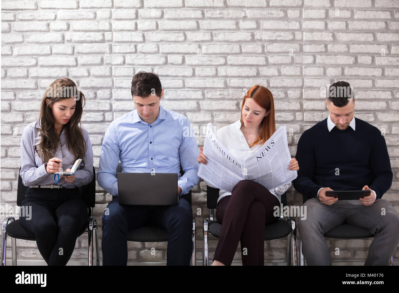 Group Of Candidate Sitting On Chair Waiting For Job Interview Against White Brick Wall Stock Photo