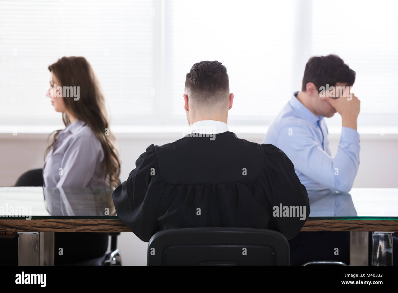 Displeased Couple Sitting In Front Of Judge At Courtroom Stock Photo