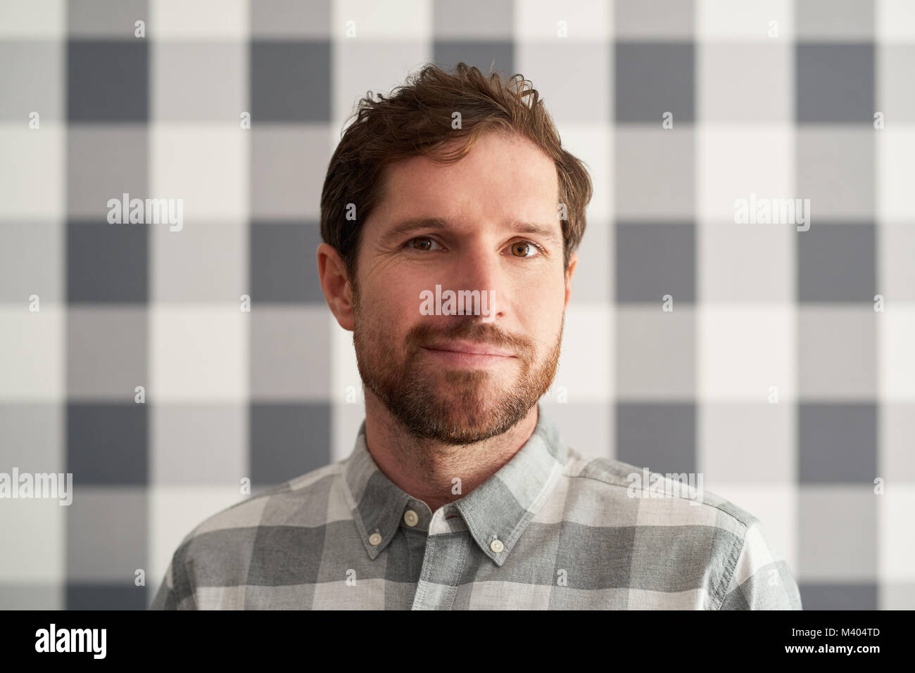 Smiling young man wearing a shirt matching his checkered wallpaper Stock Photo