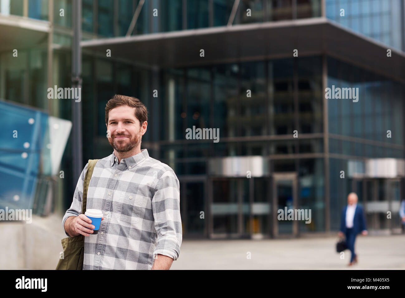 Smiling young man standing in the city drinking coffee   Stock Photo