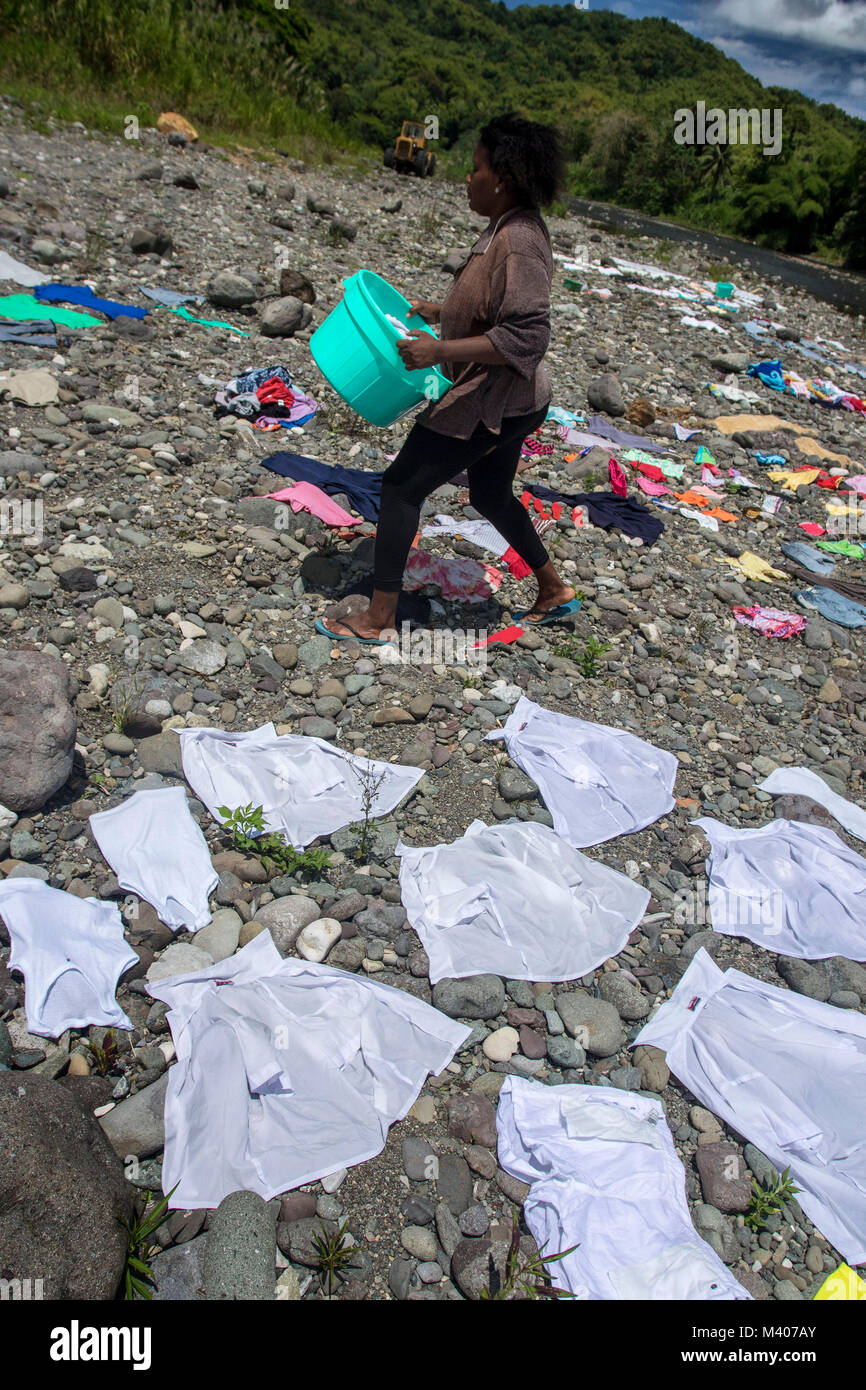 Woman in silhouette laying laundry out to dry on pebbly shore of the