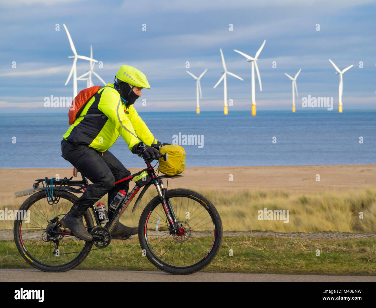 A man riding a off road sports sports bicycle in front of the Redcar Windfarm at Teesmouth Stock Photo