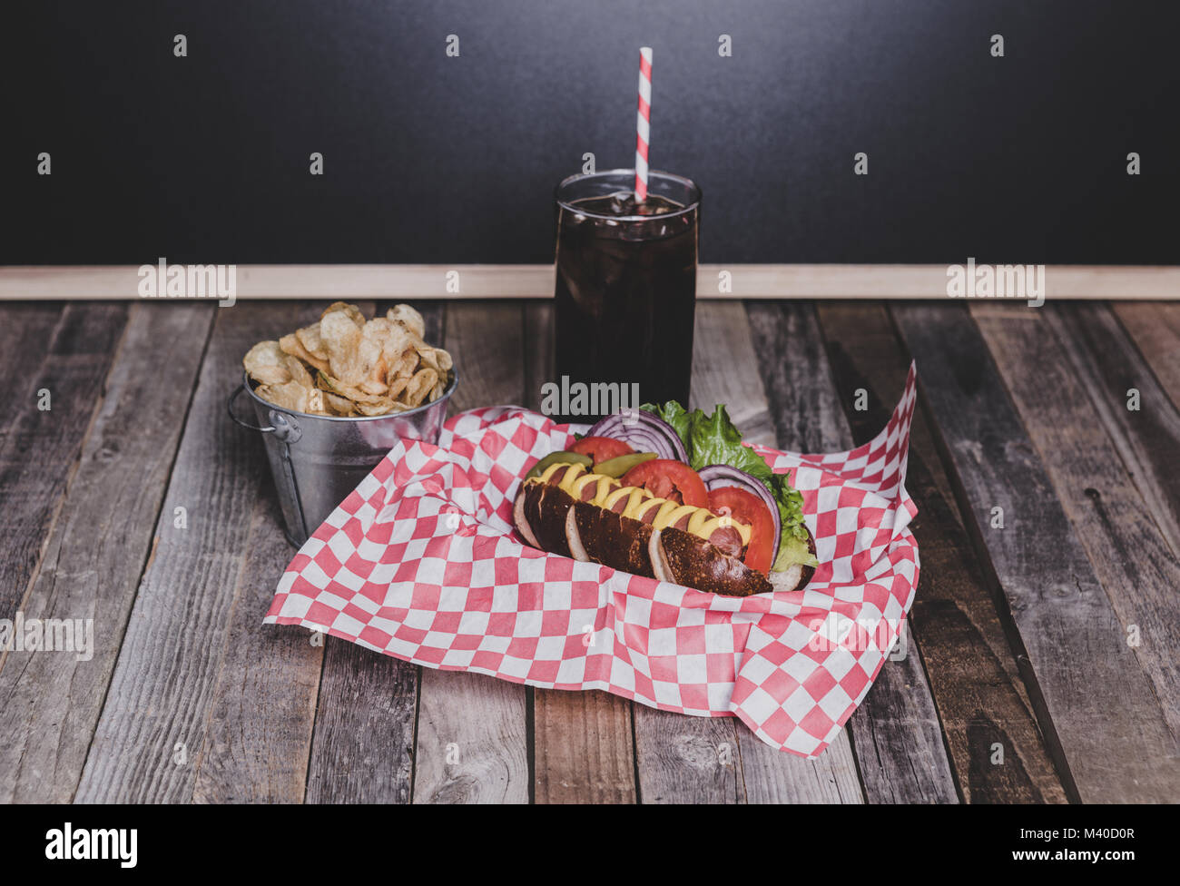Gourmet hot dog with chips and drink in a basket with gingham napkin. Tabletop, front view. Stock Photo