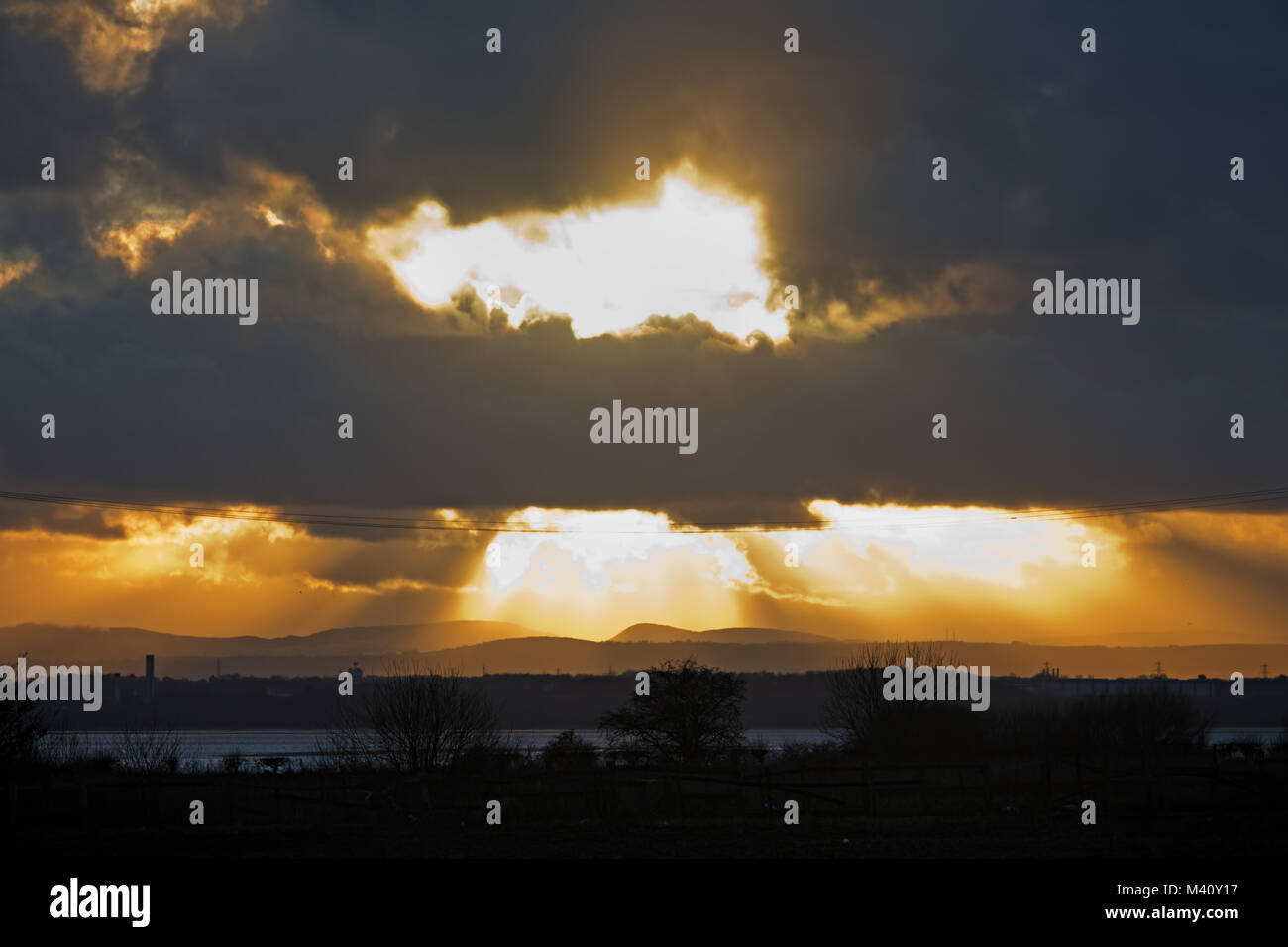 Sun bursts through stormy clouds at sunset over the River Mersey Liverpool UK. Stock Photo