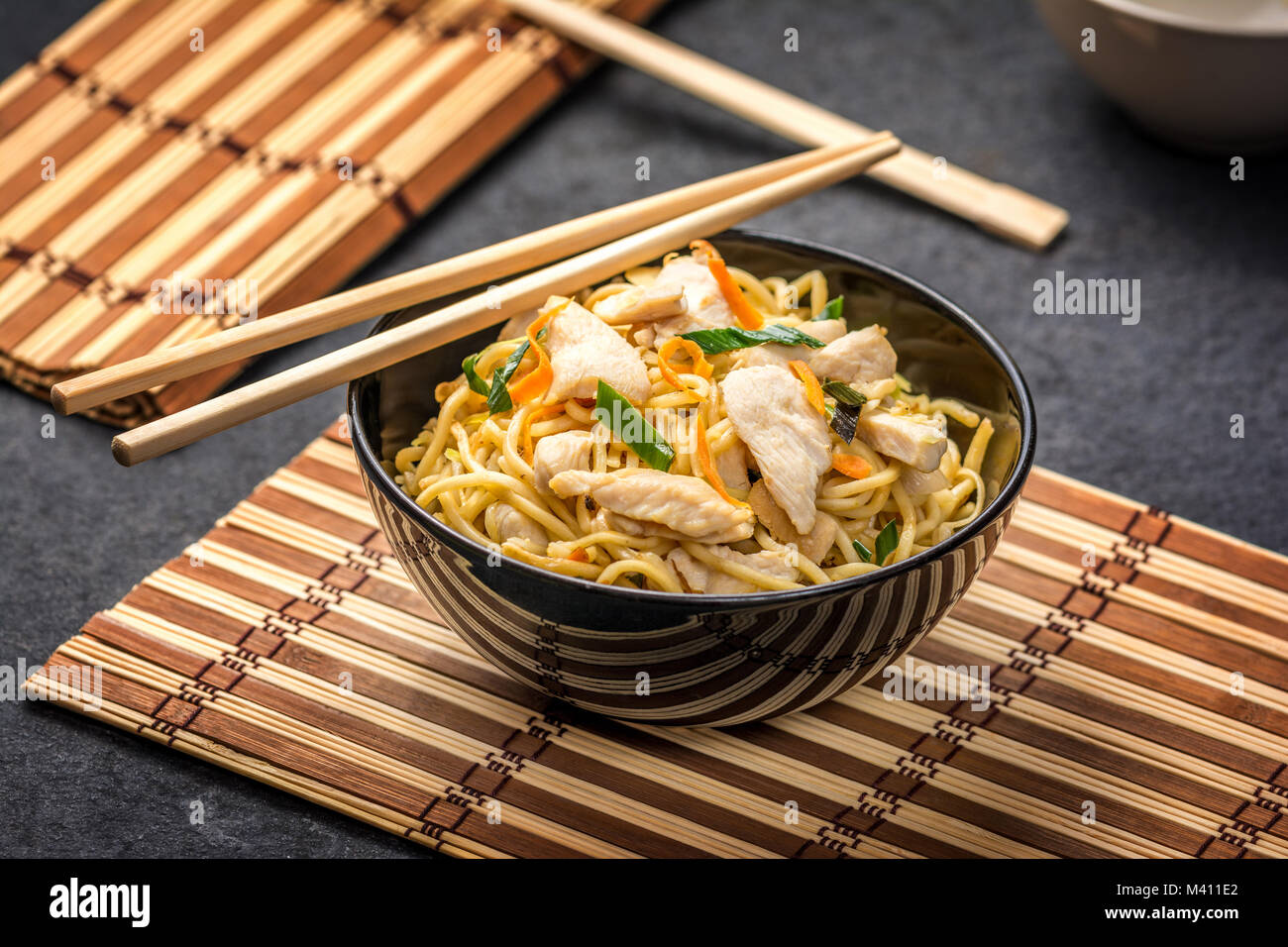 Traditional asian or chinese noodles with chicken and vegetablesin black plate and wood chopsticks on dark stone table Stock Photo