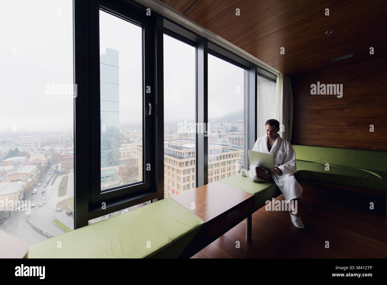Handsome young businessman wearing bath robe on the bed with laptop in  modern room. Self-employed person using laptop in penthouse and looking at  sunn Stock Photo - Alamy