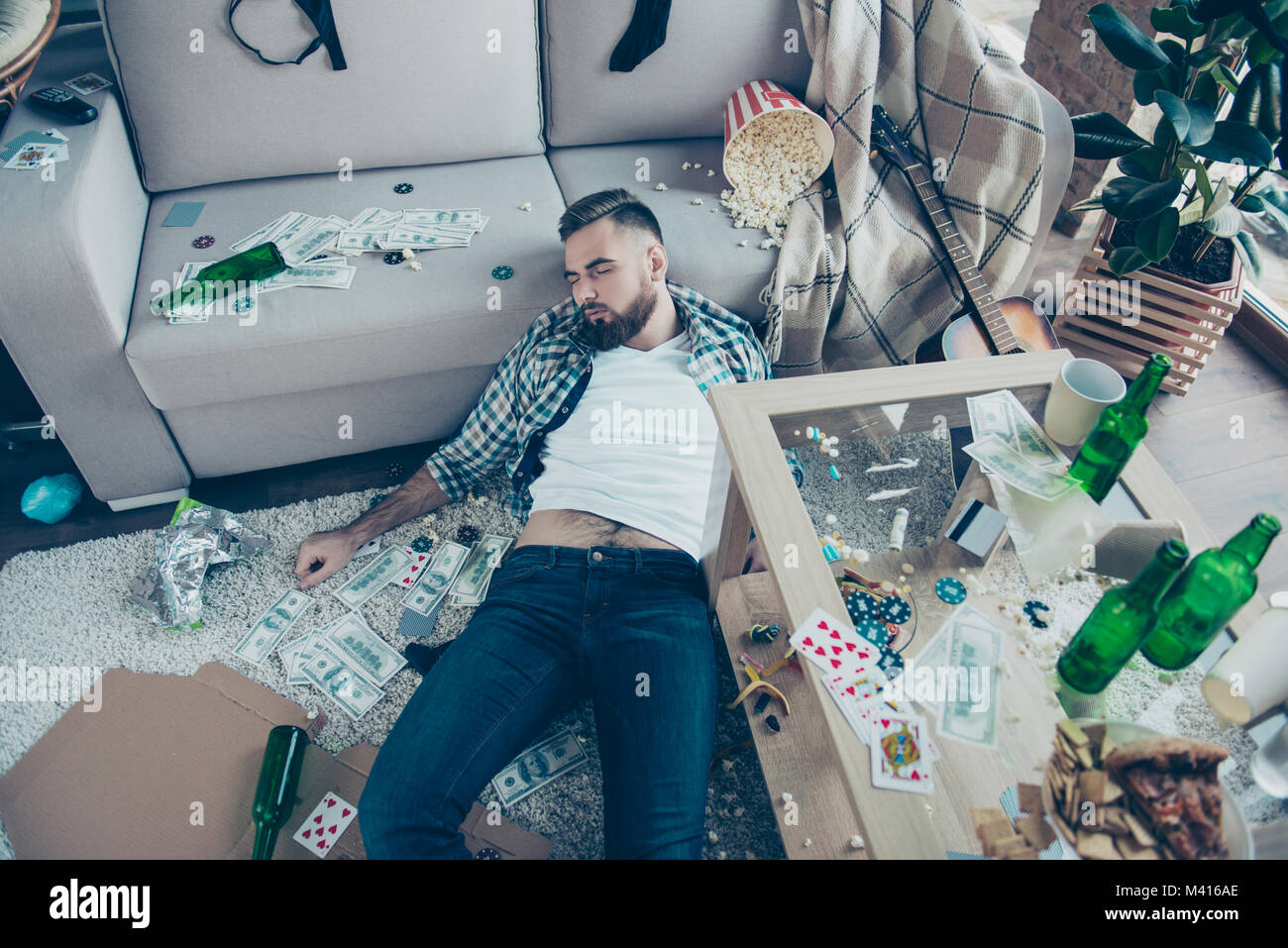 After party consequences. Top view above photo of drunk bearded wearing checkered shirt and jeans, he is sleeping on the floor and surrounded by money Stock Photo