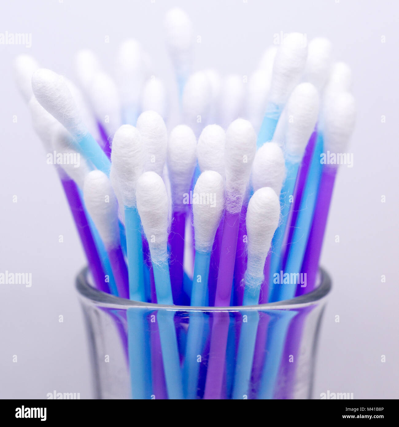 Upright purple and blue cotton buds in a small glass jar. Stock Photo