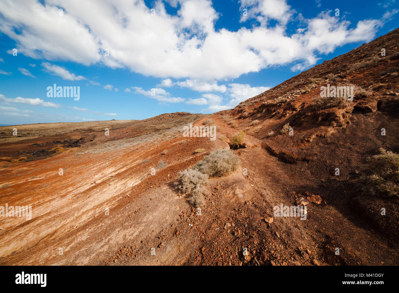 Amazing vulcanic landscape with mountains. Sky is blue with clouds, gravel is red and brown. Fuerteventura Island, Canary Island, Spain, Europe. Stock Photo