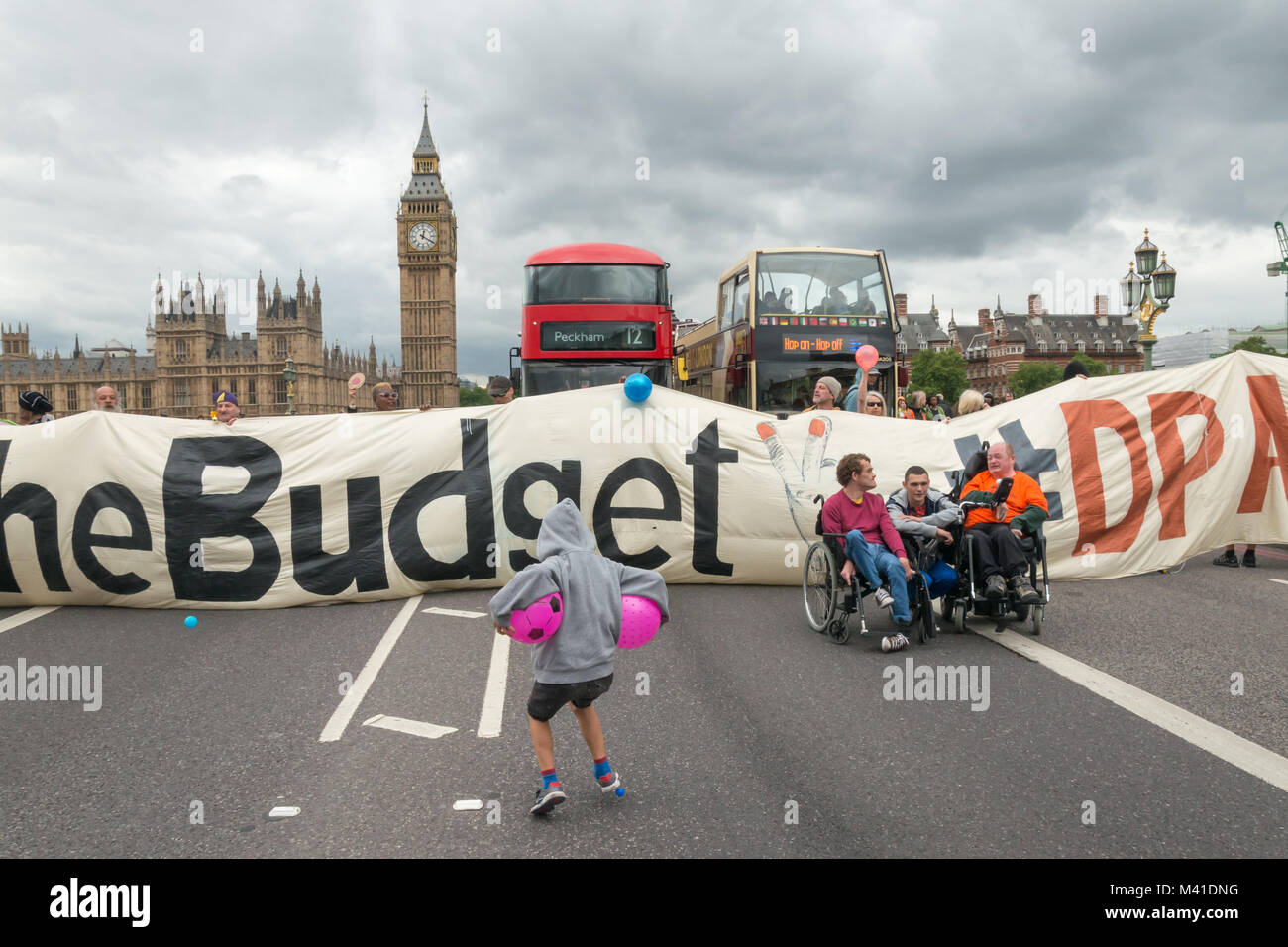 Wheelchair protesters and a boy with two pink ballsand a 23m banner '#Balls2thebudget #DPAC'  stretched across Westminster Bridge in front of the Houses of Parliament and blocked traffic in Disabled People Against the Cuts Budget Day protest. Stock Photo