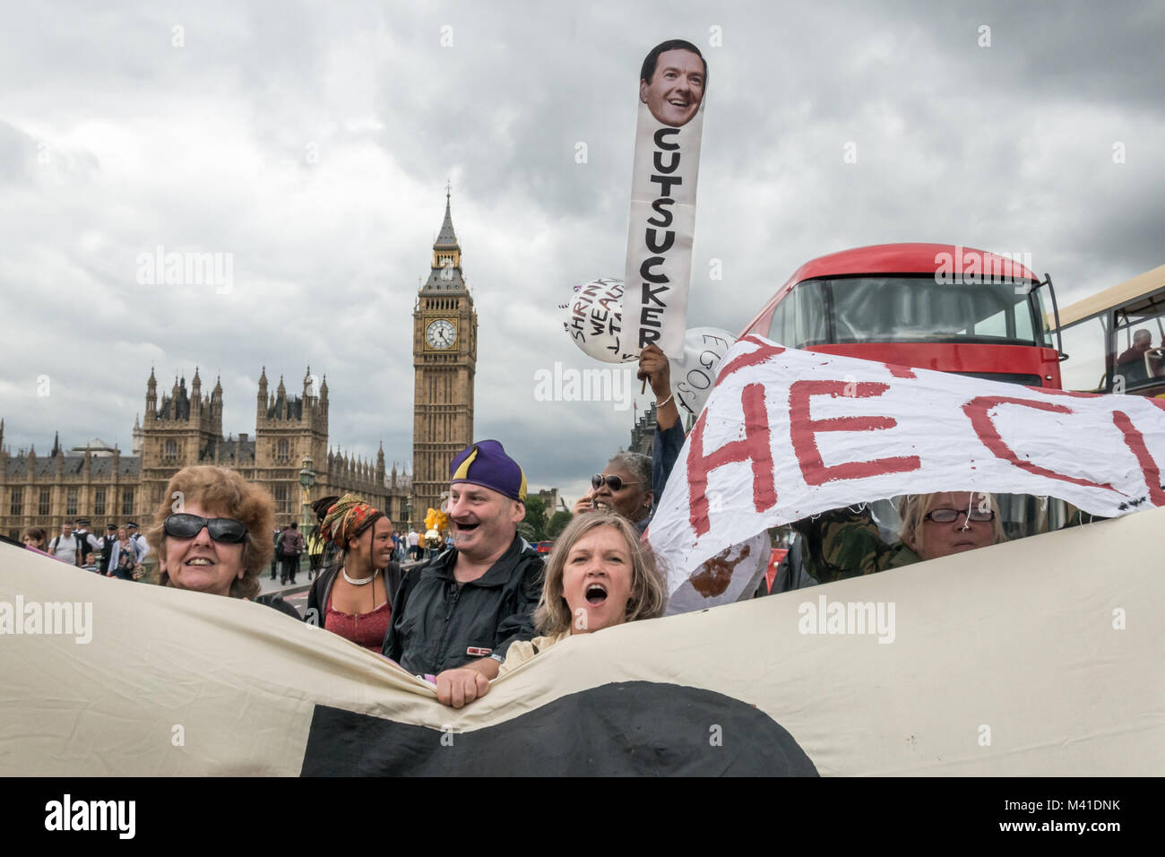 A woman holds up a placard with a picture of George Osbone and the word 'CUTSUCKER' with two balloons behind the DPAC Banner blocking traffic on Westminster Bridge on Budget Day in protest against cuts hitting the disabled. Stock Photo