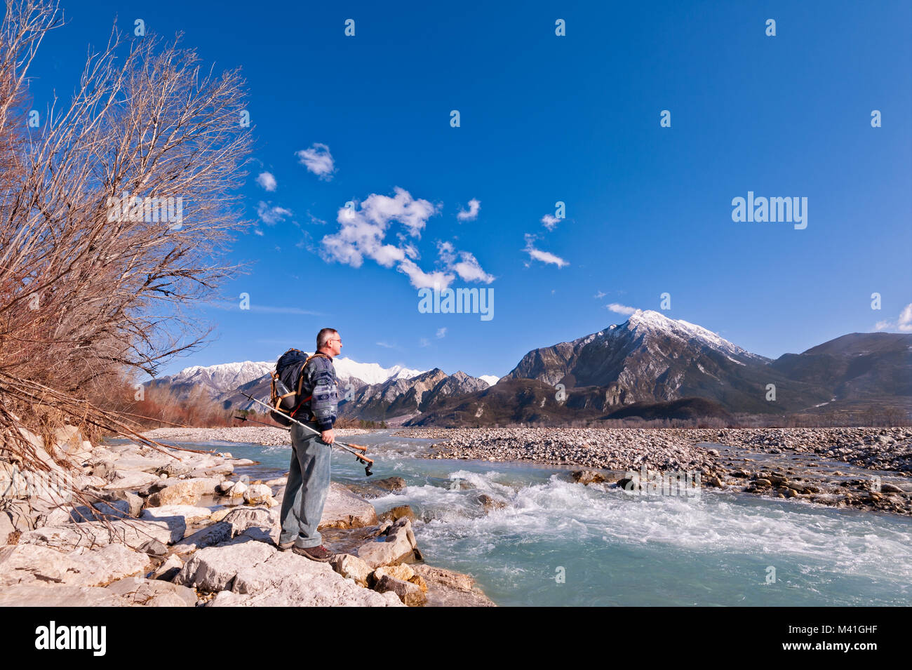 Hiker standing on river shore, looking the mountains landscape. Alps,Italy,Friuli. Stock Photo