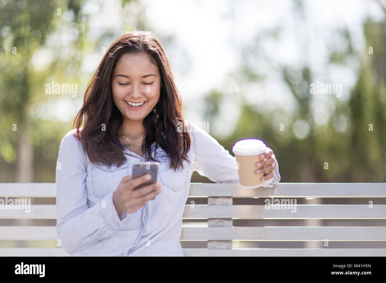 Woman sitting on bench checking smartphone Stock Photo