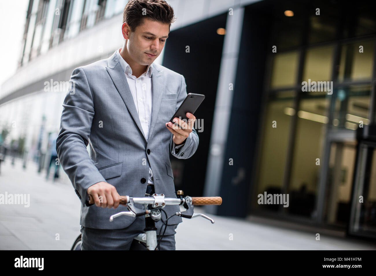Businessman cycling to work using smartphone Stock Photo