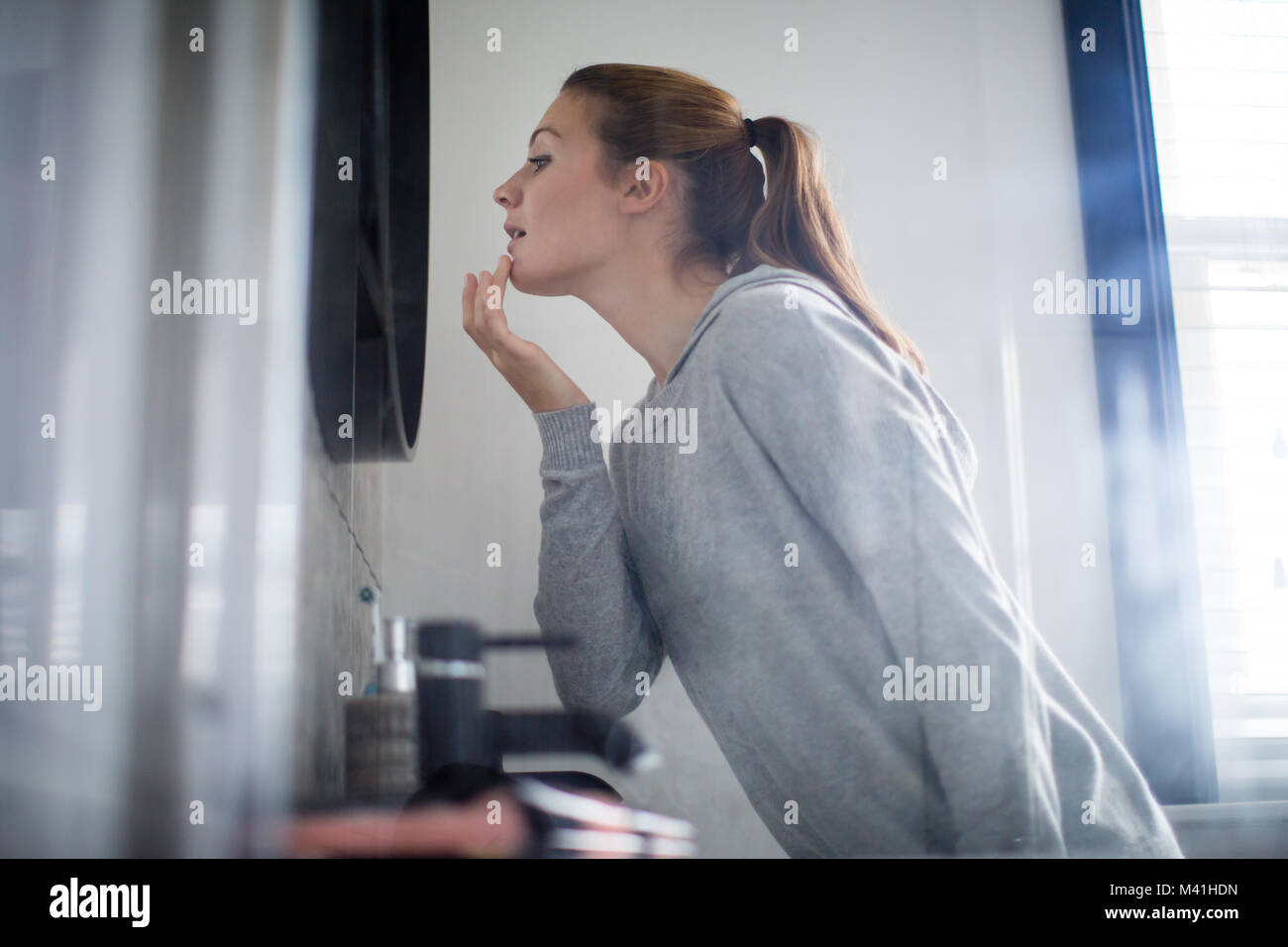 Young adult female putting looking at reflection in bathroom mirror Stock Photo