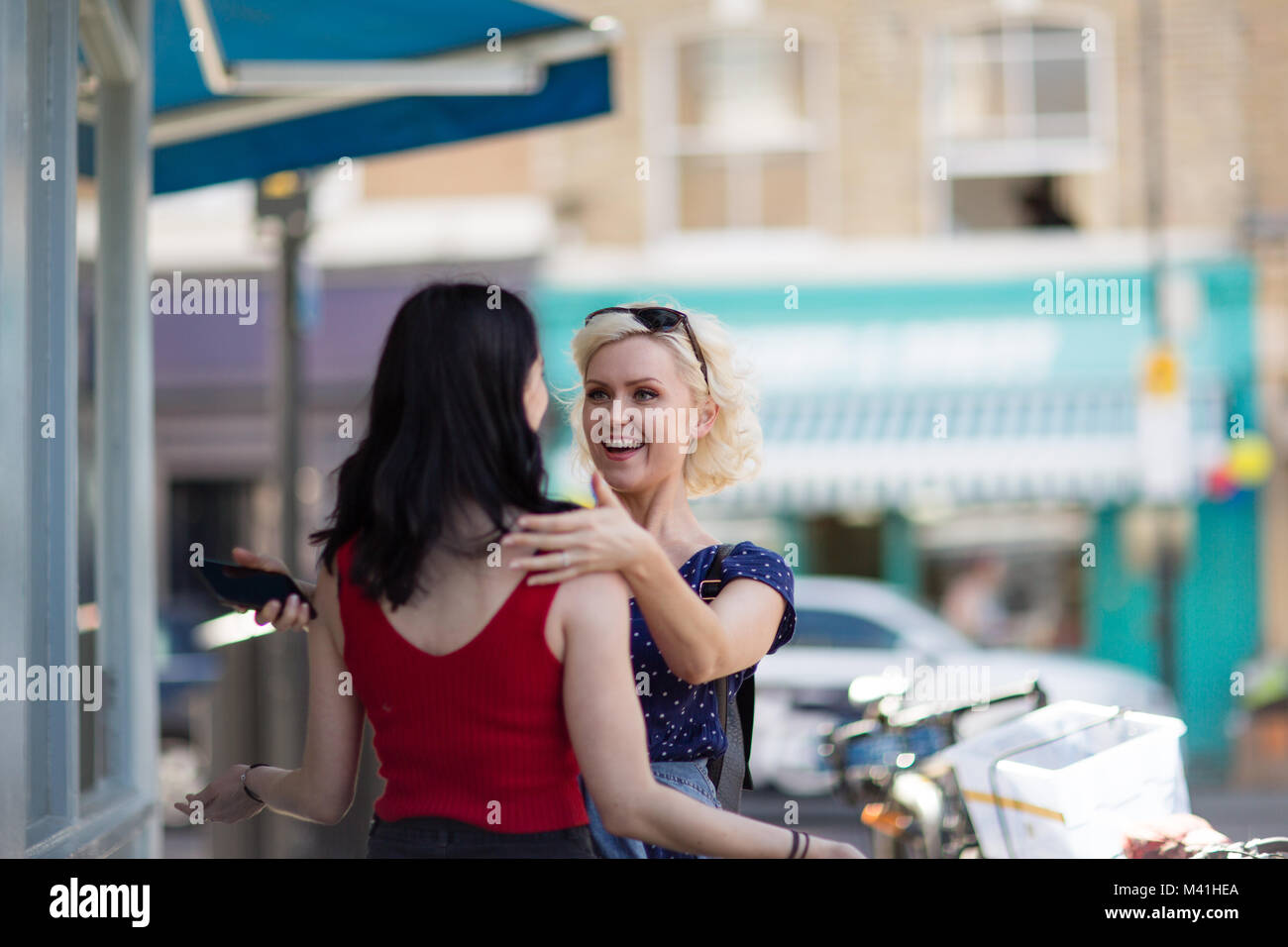 Female friends meeting outdoors on shopping street Stock Photo