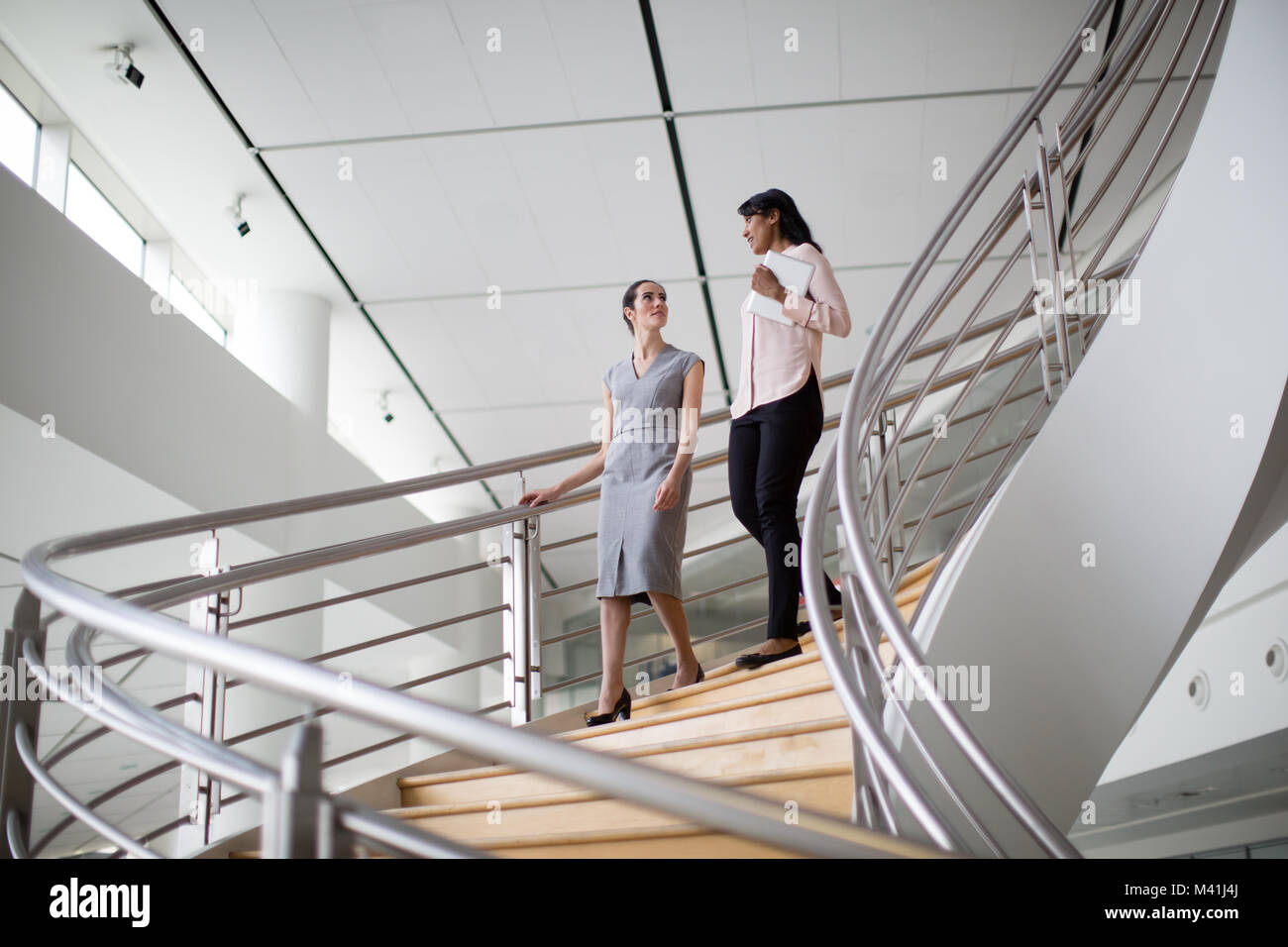 Female business colleagues walking down spiral staircase Stock Photo