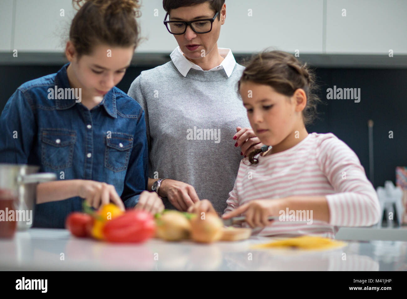 Mum teaching daughters to chop vegetables Stock Photo