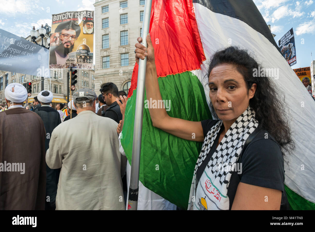 A Palestinian woman carries a large pole with several Palestinian flags on it on tthe Al Quds Day march in London. Stock Photo