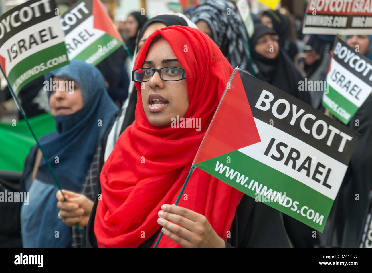 A woman in a red headscarf carries a 'Boycott Israel' Palestinian flag ...