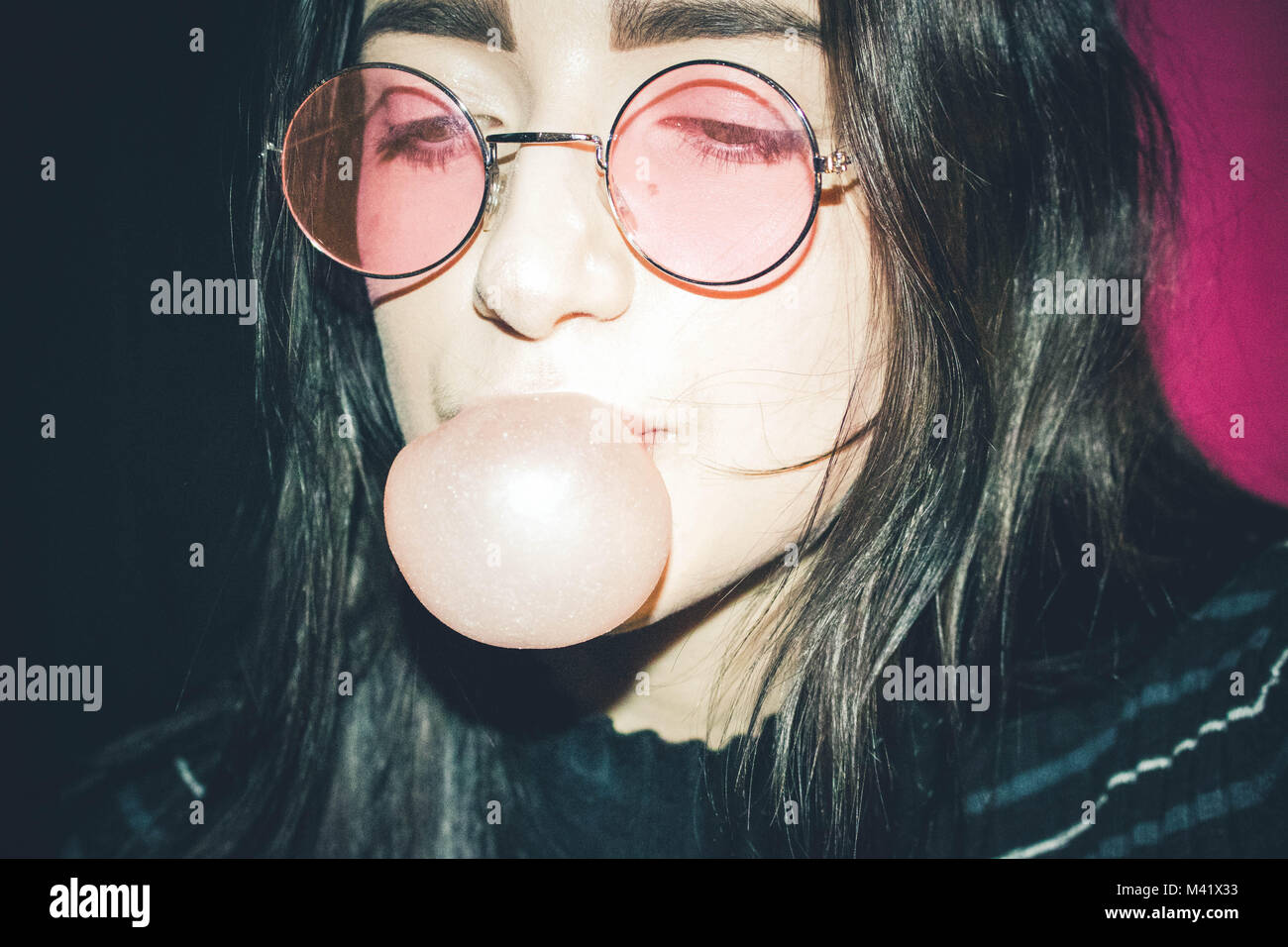 Girl in pink sunglasses blowing a bubble Stock Photo