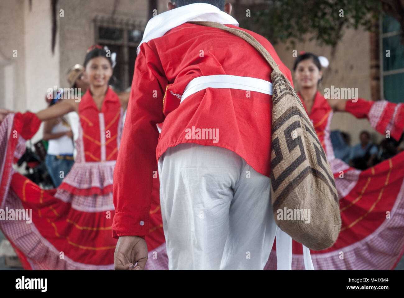 A man wearing traditional red and white clothing dancing with two women wearing dresses at Barranquilla Carnival Stock Photo