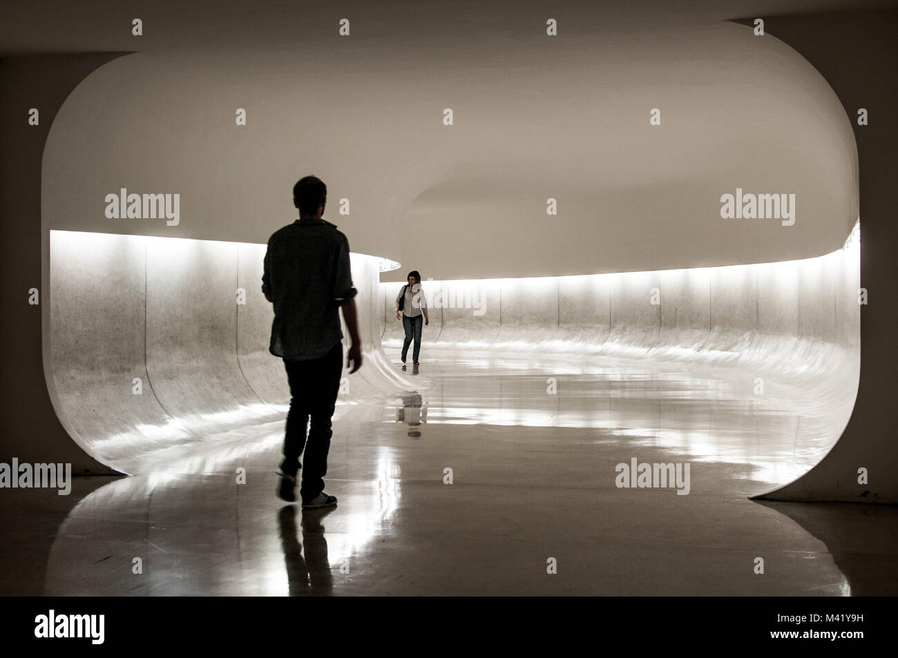A young man and woman walking towards each other and about to cross paths in a tunnel inside a museum in Curitiba, Brazil Stock Photo