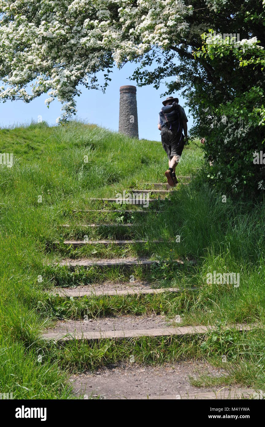 A hiker with a rucksack walking up stone steps in a park with a brick chimney in the background Stock Photo