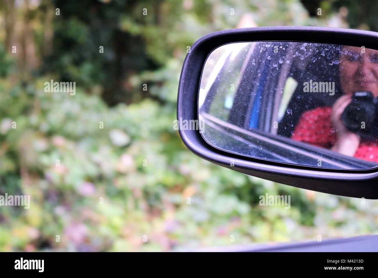 Image of smiling woman taking selfie with camera in reflection of dirty car wing mirror Stock Photo