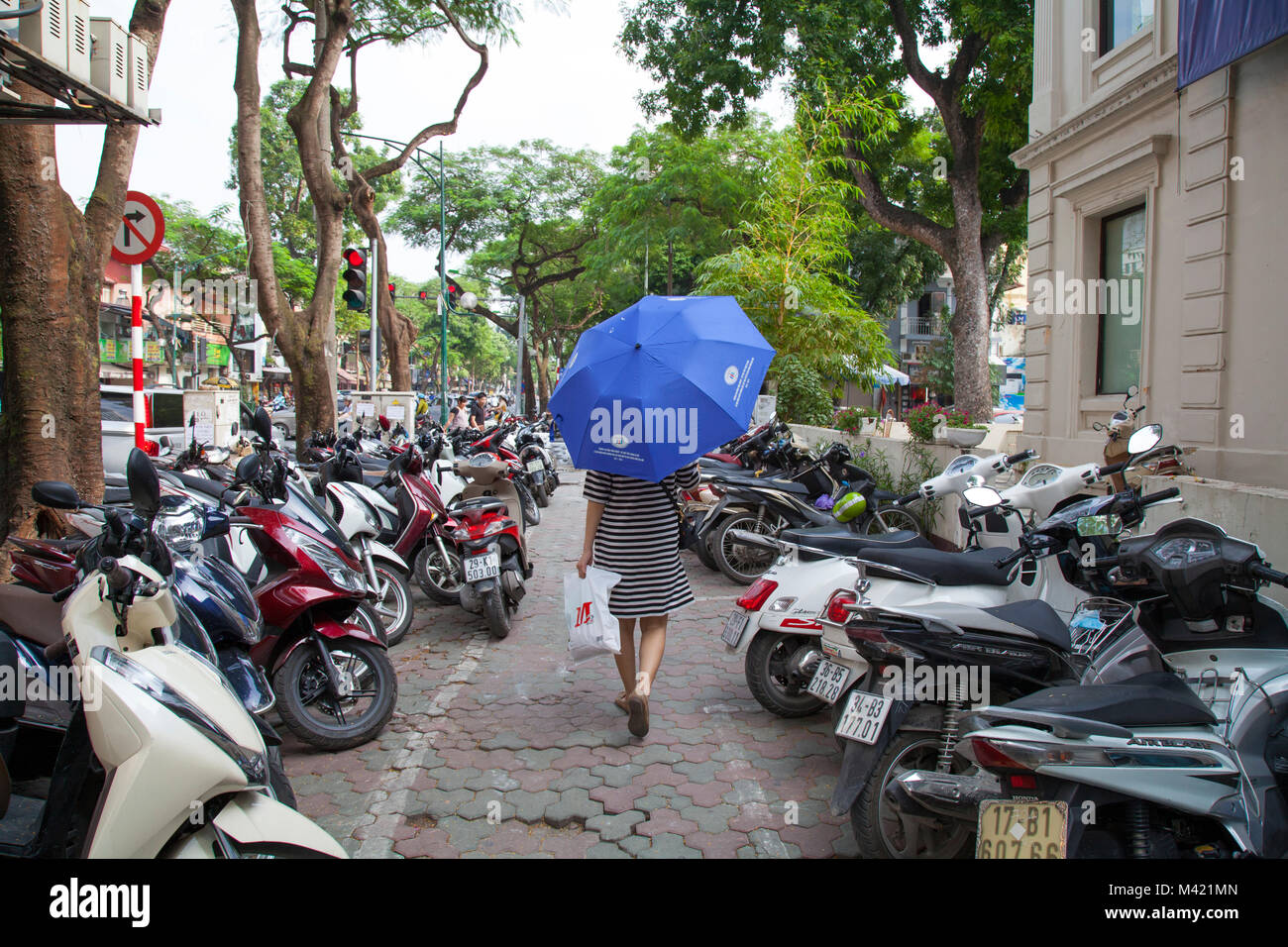 Woman with umbrella for shade walking down the sidewalk street in Hanoi