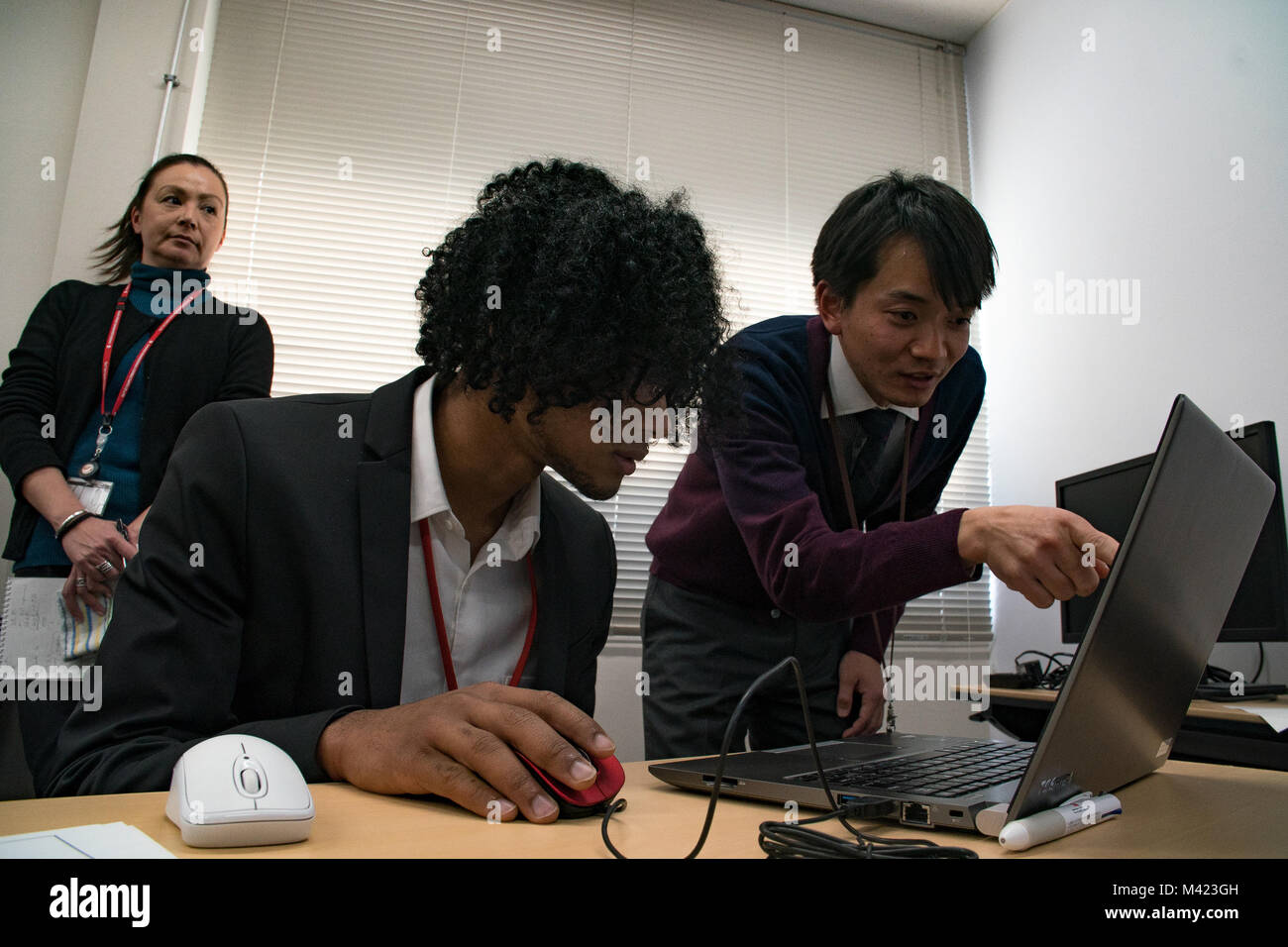 Kenzo Tanaka, right, an architectural engineer with Chuden Engineering Consultants (CEC), helps David Shoebrook, a Matthew C. Perry High School student from Marine Corps Air Station Iwakuni, Japan, while using an architectural computer program at CEC’s facility in Hiroshima, Feb. 8, 2018. The Defense Policy Review Initiative (DPRI) scheduled a day with CEC to host their first American visitors, which included five Matthew C. Perry High School students, DPRI employees and a Matthew C. Perry teacher, for a tour of the building and to visit with their employees to see how they work. (U.S. Marine  Stock Photo