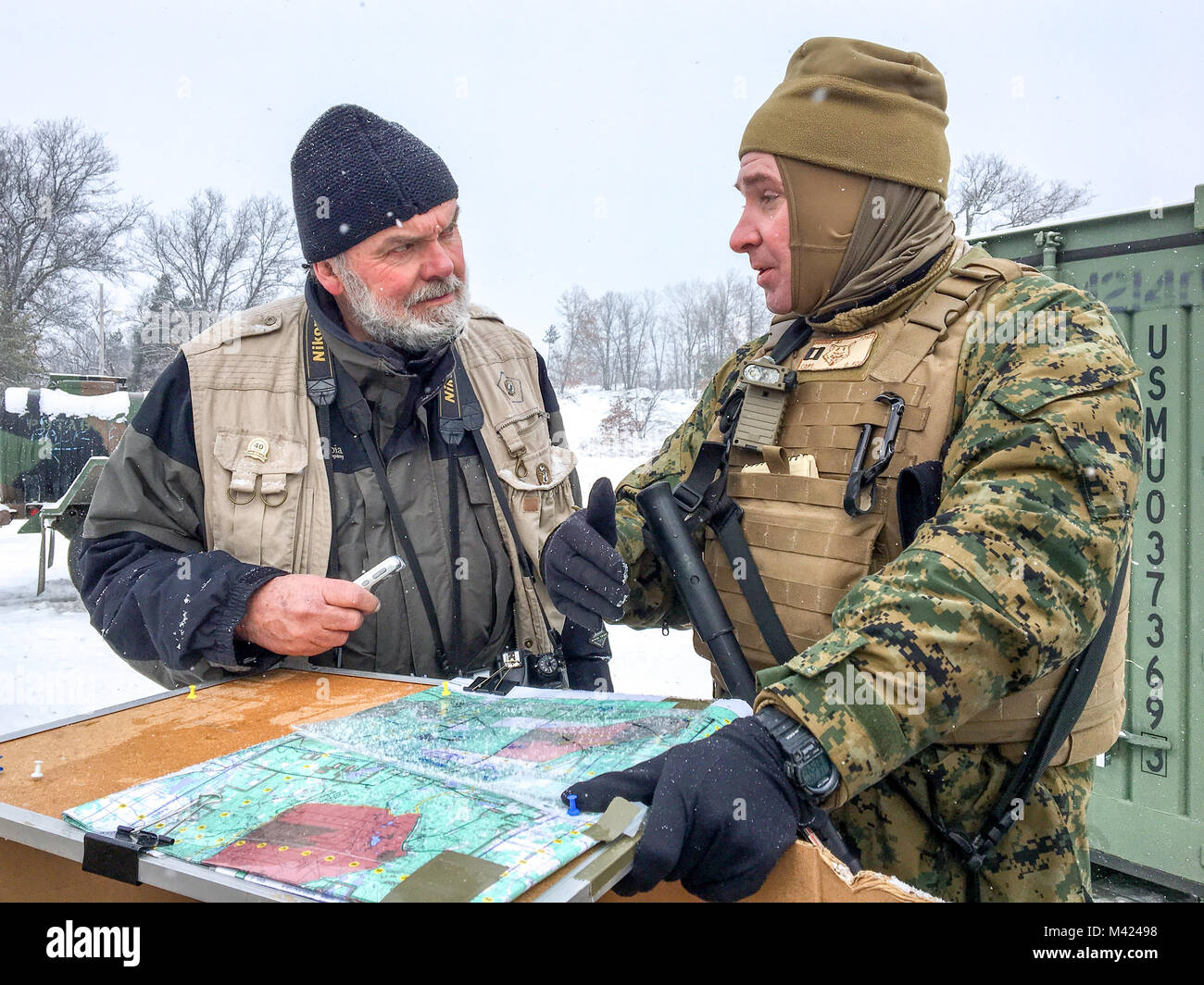 John Russell (left), a freelance photojournalist with Detroit Free Press, talks with Capt. Andrew Bender, commanding officer of Company F, 4th Tank Battalion, 4th Marine Division, about the scheme of maneuver for Fox Co. Marines during training day three ofexercise Winter Break 2018, near Camp Grayling, Feb. 9, 2018. During Winter Break 18, the Camp Lejeune, North Carolina, based tank company is taking advantage of Camp Grayling’s rugged training areas to test their offensive, defensive and maneuver capabilities in an austere cold weather environment. Stock Photo