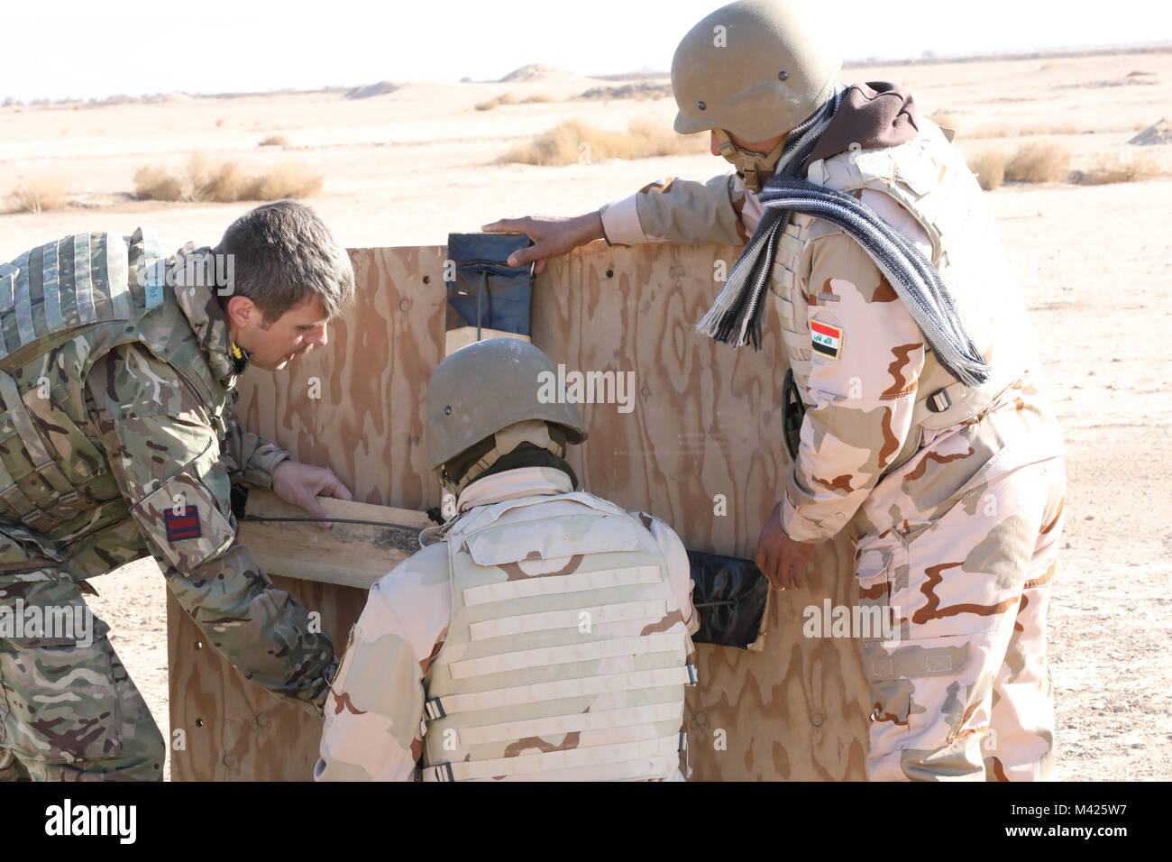 A British army engineer and students assigned to the 38th Brigade, Iraqi army, mount their breaching devices onto plywood as a simulated door at the demolition soldier assault course on the Besmaya Range Complex, Iraq, Jan. 29, 2018.  More than 74 Coalition members have committed themselves to the goal of eliminating the threat posed by ISIS in Iraq and Syria and have contributed in various capacities to the effort. (U.S. Army photo by Master Sgt. Horace Murray) Stock Photo