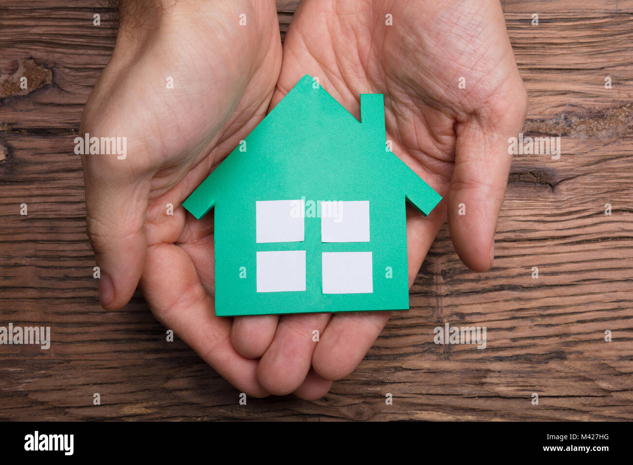 Close-up Of Hands Holding Paper House Against Wooden Table Stock Photo