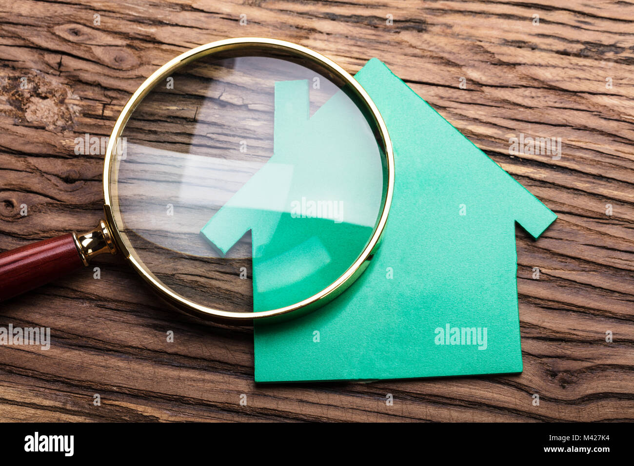 Closeup Of Magnifying Glass And Green Paper House On Wood Stock Photo