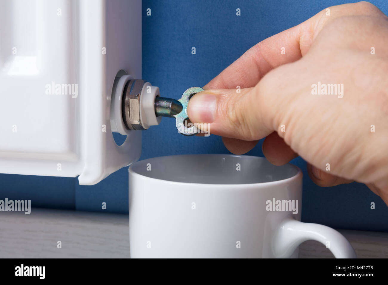 Close-up Of Person's Hand Turning Radiator Bleed Valve To Release Air With Cup At Home Stock Photo