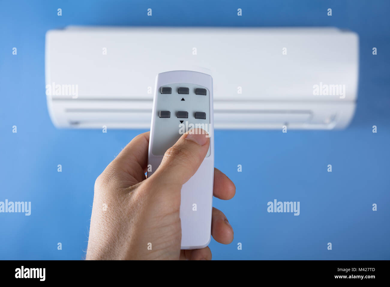 Close-up Of Man's Hand Adjusting Temperature Of Air Conditioner Using Remote Stock Photo