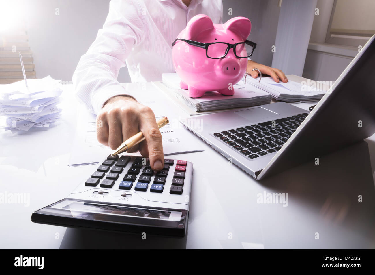 Midsection Of Businessman Calculating Tax Using Calculator With Piggybank And Laptop On Desk In Office Stock Photo