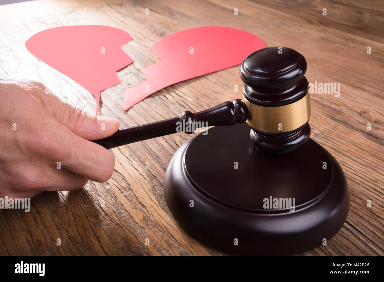 Cropped Image Of Divorce Judge With Broken Heart At Desk Hitting Gavel In Courtroom Stock Photo
