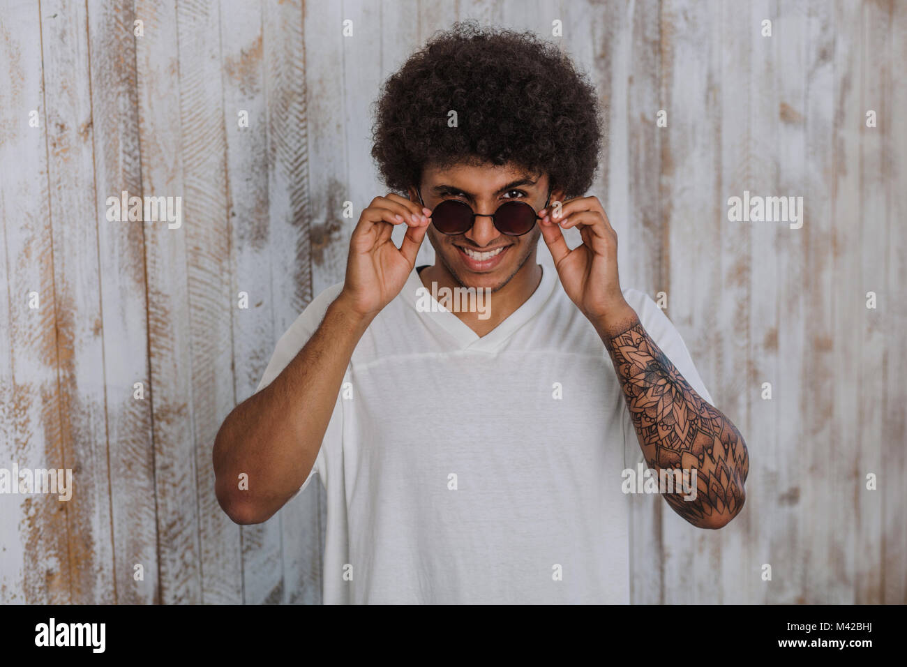 Smile!portrait  curly and an African man  adjusting his sunglasses and winks. while standing against old wooden background Stock Photo