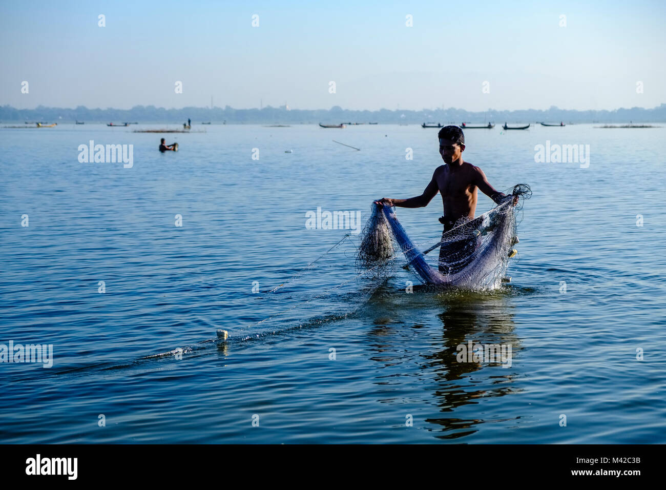 A fisherman, standing in the shallow water of Taungthaman Lake, is pulling his net out Stock Photo