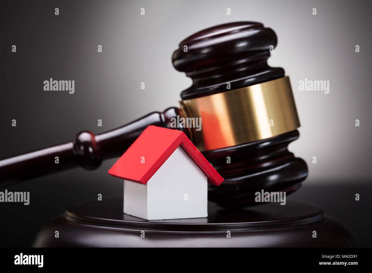 Close-up Of Gavel And House Model On Sounding Block Against Grey Background Stock Photo