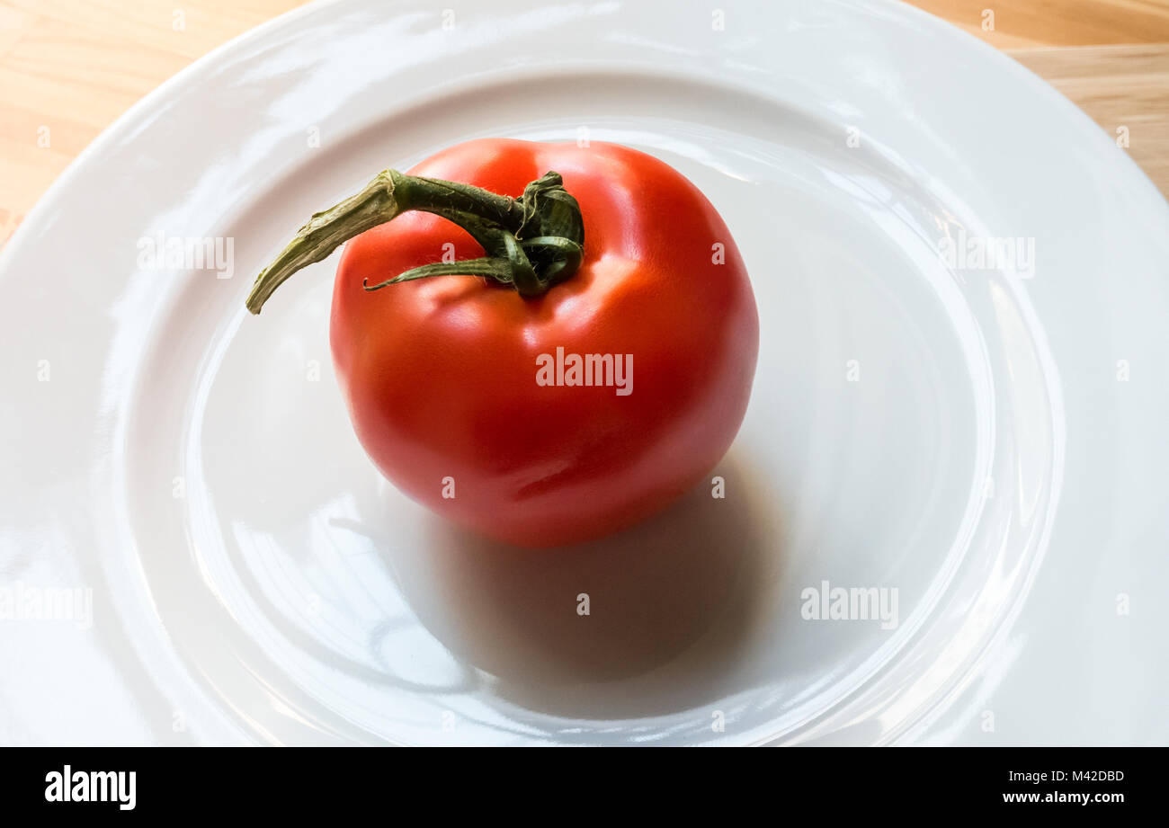 A Large vine-ripened tomato on a white plate Stock Photo