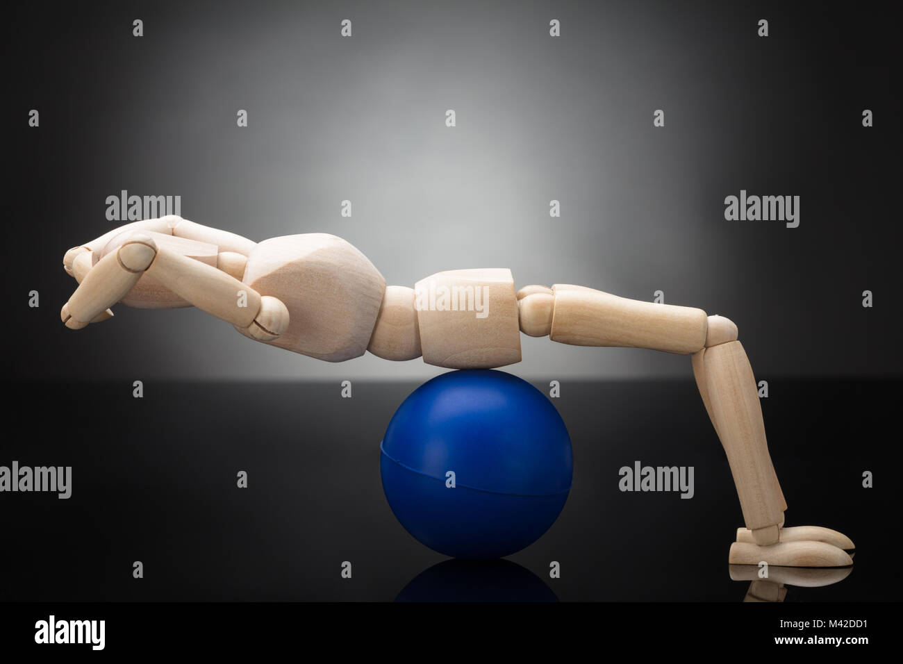 Side View Of A Wooden Dummy Doing Workout On Fitness Ball Against Grey Background Stock Photo