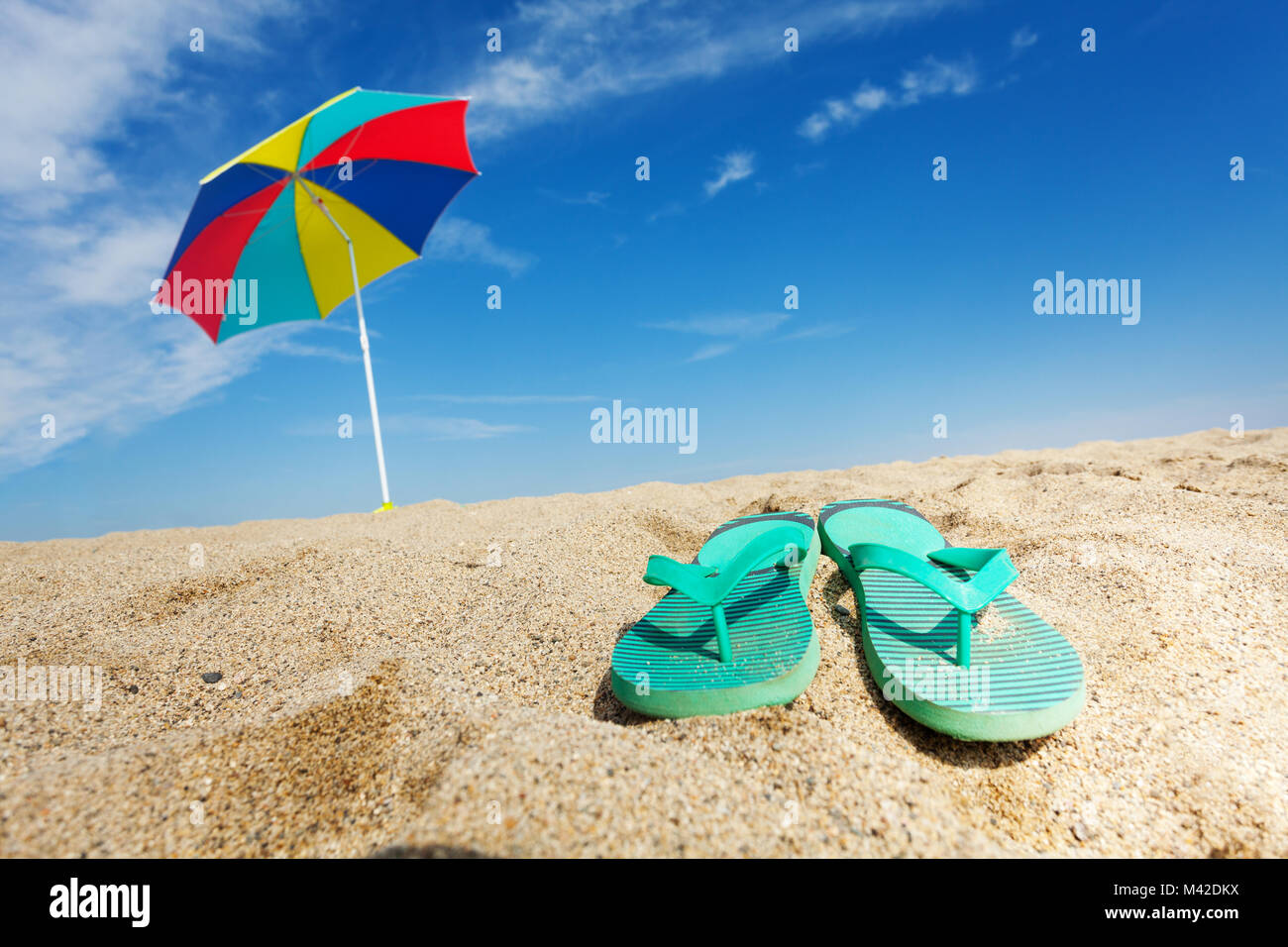 Tropical background with flip flops and sun umbrella on the sandy beach ...
